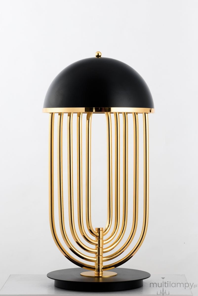 Lampa stołowa Dolce Vita w kolorze czarnym i złotym, z okrągłym kloszem i metalowymi rurkami w złotym wykończeniu. Ułożona na okrągłej podstawie, o nowoczesnym designie, idealna do stylowych wnętrz. Wysokość lampy umożliwia efektywne oświetlenie.