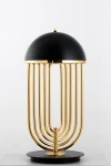 Lampa stołowa Dolce Vita w kolorze czarnym i złotym, z okrągłym kloszem i metalowymi rurkami w złotym wykończeniu. Ułożona na okrągłej podstawie, o nowoczesnym designie, idealna do stylowych wnętrz. Wysokość lampy umożliwia efektywne oświetlenie.