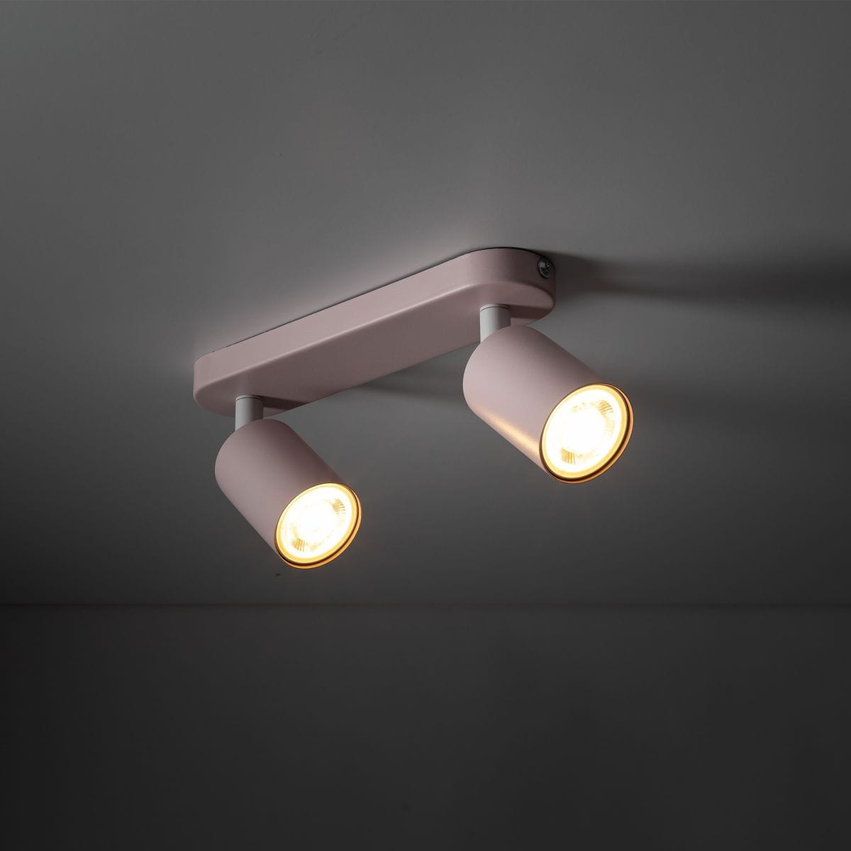 Lampa sufitowa Livia w kolorze różowym z dwoma reflektorami GU10. Elementy są metalowe, zamontowane na prostokątnej podstawie. Reflektory skierowane są lekko na zewnątrz, emitując ciepłe światło.