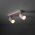 Lampa sufitowa Livia w kolorze różowym z dwoma reflektorami GU10. Elementy są metalowe, zamontowane na prostokątnej podstawie. Reflektory skierowane są lekko na zewnątrz, emitując ciepłe światło.