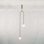 Lampa wisząca Loop 2xG9 w kolorze złotym, z dwiema okrągłymi, białymi kloszami, zawieszona na długim, cienkim ramieniu. Produkt pokazany z przodu na jednolitym tle, podkreślający nowoczesny design i elegancki styl.