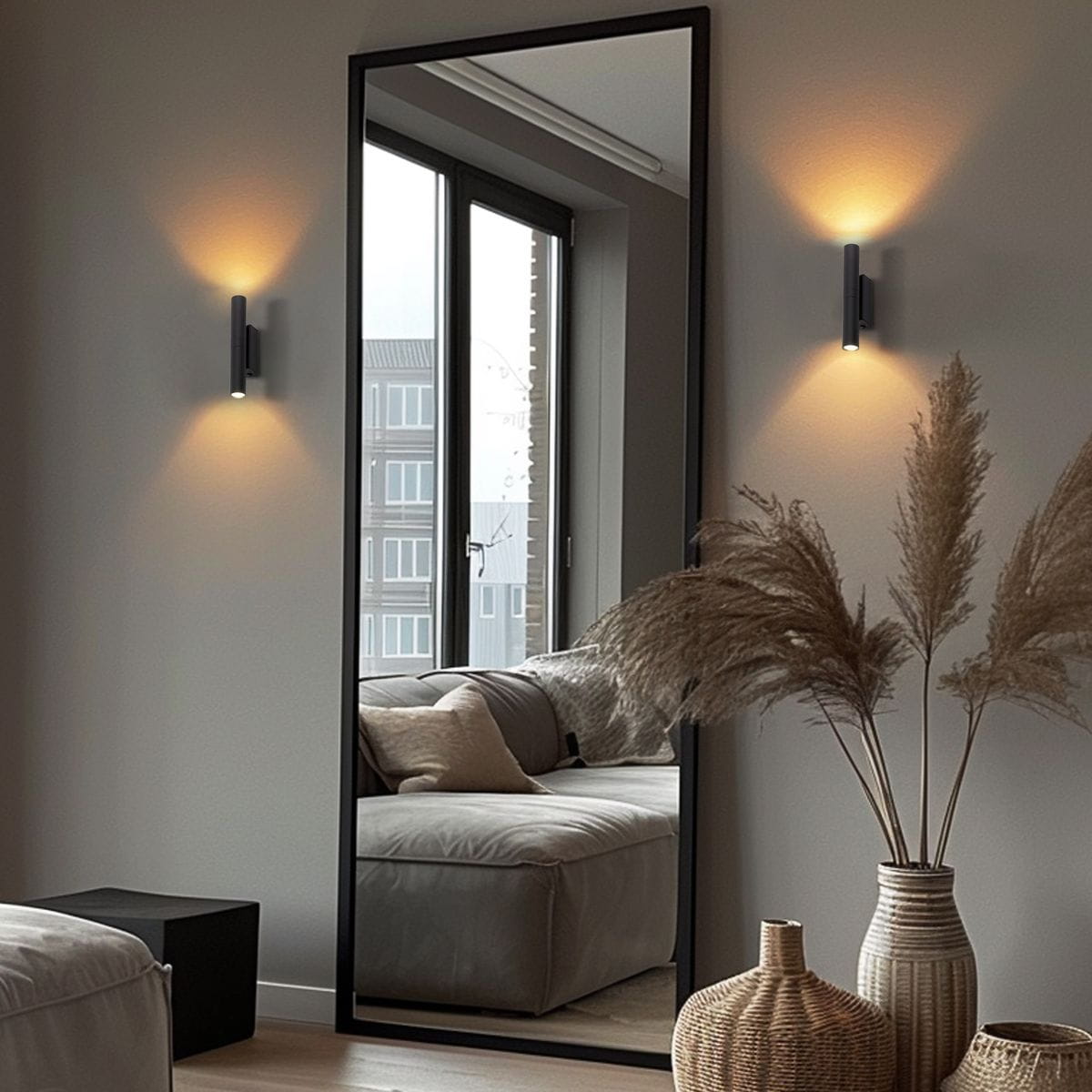 Kinkiet Lagos 2xG9 w kolorze czarnym montowany na ścianie, emituje ciepłe światło w górę i w dół. Minimalistyczny design, widoczny w nowoczesnym wnętrzu z lustrem, sofą i dekoracyjnymi roślinami.