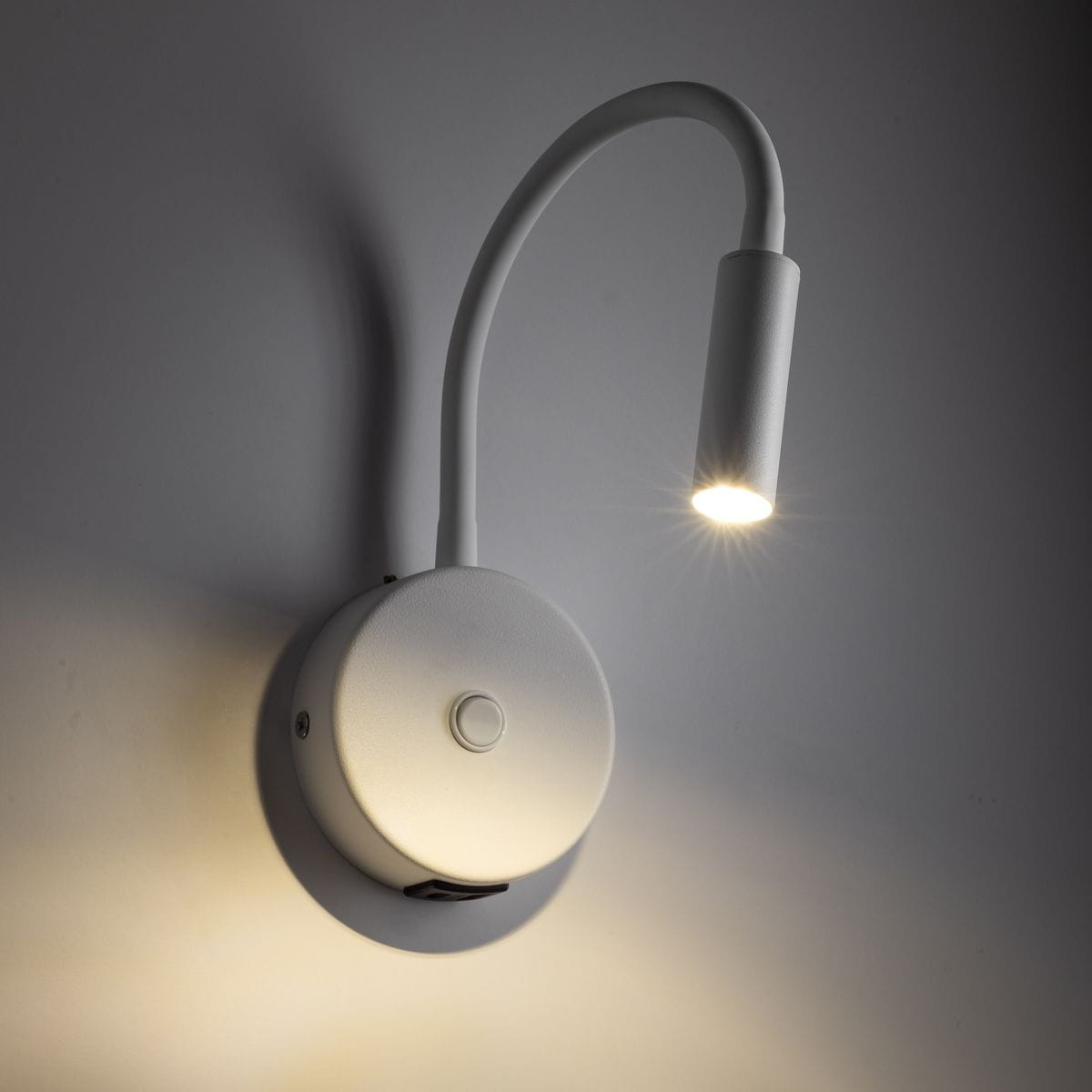 Biały kinkiet Lagos z giętkim ramieniem i oprawą G9. Posiada wbudowane gniazdo USB. Ujęcie frontalne, produkt zamontowany na ścianie, z widoczną włącznikiem. Jasne światło emitowane z końcówki lampy.