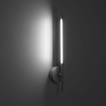 Kinkiet Focus 2xLED/4W +1W w kolorze białym, zamontowany na ścianie. Posiada prostą, cylindryczną formę z metalowym uchwytem oraz długą, prostą oprawę świetlną, emitującą jasne światło. Tło w odcieniu szaro-białym.