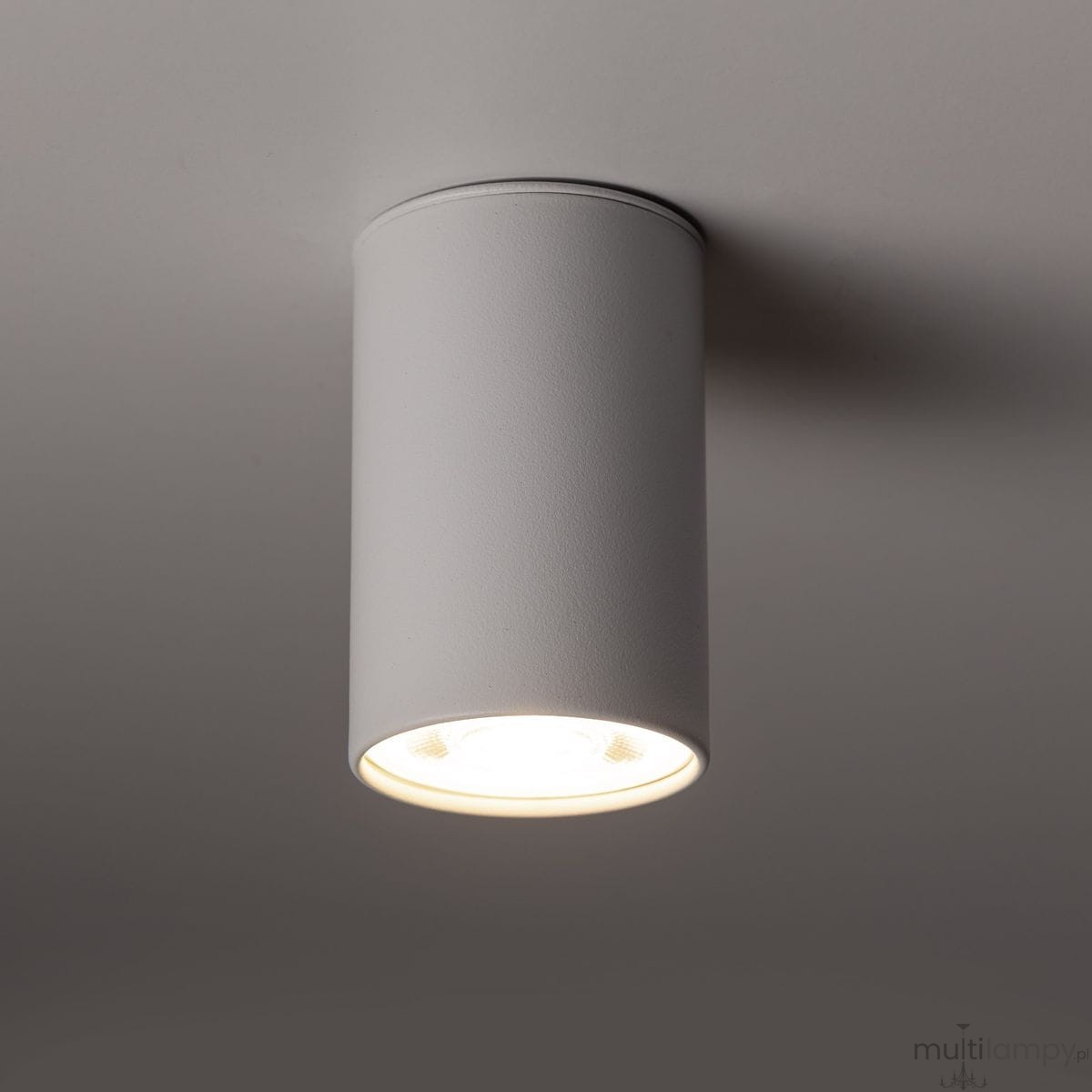 Lampa sufitowa w kolorze białym, cylindryczna, z pojedynczym źródłem światła GU10. Ujęcie z dołu, ukazujące górną część lampy oraz otwór emitujący światło. Tekstura matowa, montowana na suficie.