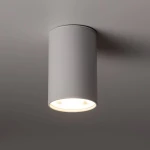 Lampa sufitowa w kolorze białym, cylindryczna, z pojedynczym źródłem światła GU10. Ujęcie z dołu, ukazujące górną część lampy oraz otwór emitujący światło. Tekstura matowa, montowana na suficie.