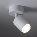 Lampa sufitowa w białym kolorze, z pojedynczym spotem, montowana na suficie. Cylindryczny kształt oprawy, z widoczną żarówką GU10. Ujęcie z boku, pokazujące detal konstrukcji i źródło światła.