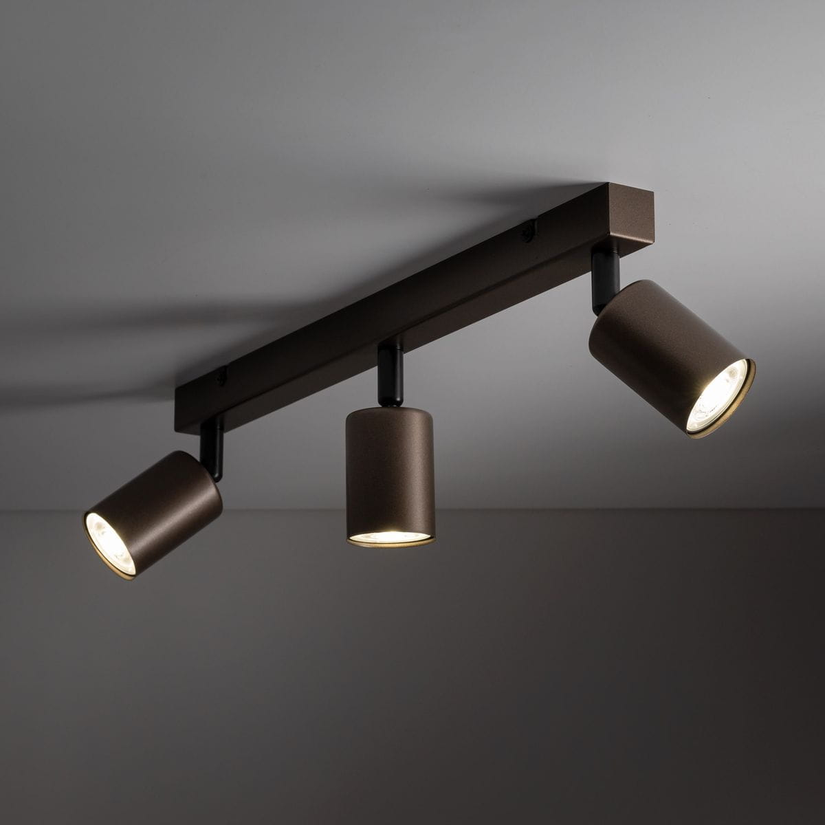 Brązowa lampa sufitowa typu spot z trzema reflektorami GU10. Ujęcie z przodu, montowana na suficie. Reflektory mają cylindryczny kształt, a całość wyróżnia się matową powierzchnią. Idealna do oświetlenia wnętrz.