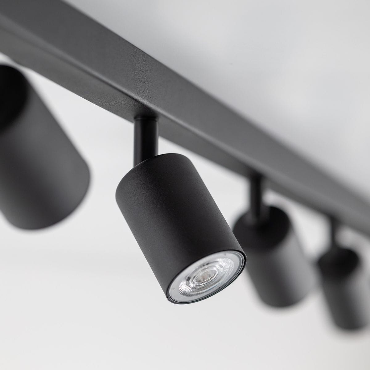 Czarna lampa sufitowa typu spot z osiemnastoma gniazdami GU10. Ujęcie z dołu, pokazujące detale cylindrycznych kloszy oraz metalowej konstrukcji. Lampa zamontowana na białym suficie, z widocznymi źródłami światła.