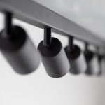 Czarna lampa sufitowa typu spot z ośmioma oprawami na żarówki GU10. Ujęcie z bliska ukazuje cylindryczne klosze zamocowane na metalowej konstrukcji. Tło białe, co podkreśla minimalistyczny design lampy.