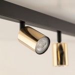 Lampa sufitowa typu spot z sześcioma oprawami GU10, w kolorze czarnym z elementami złotymi. Zbliżenie na złoty reflektor z przezroczystą soczewką, zamocowany na czarnej konstrukcji. Produkt w pozycji wiszącej, na jednolitym tle.