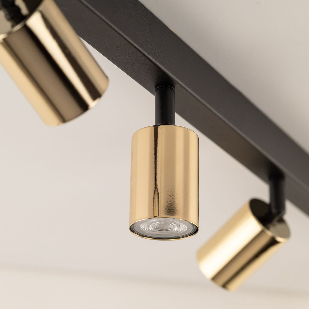 Lampa sufitowa w kolorze czarnym z sześcioma reflektorami GU10 w złotych oprawach. Ujęcie z bliska na detale złotych kloszy i czarnego stelaża. Idealna do nowoczesnych wnętrz.
