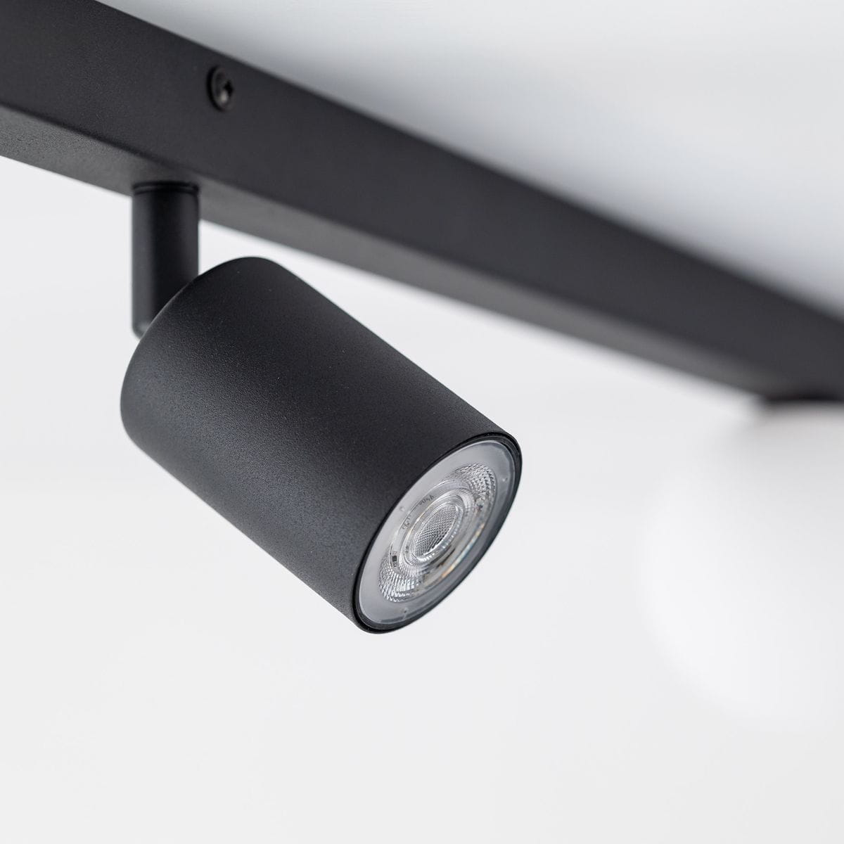 Czarna lampa sufitowa Vox z jednym źródłem światła GU10 i dwoma G9. Ujęcie z boku pokazuje cylindryczny klosz z matowym wykończeniem. Lampa zamontowana na prostokątnej podstawie, w minimalistycznym stylu, na jasnym tle.