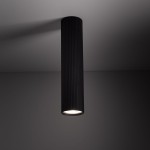 Lampa sufitowa Tune L w kolorze czarnym, cylindryczna, z podłużnymi żłobieniami. Ujęcie z dołu, pokazujące zamontowaną lampę z widocznym źródłem światła GU10. Tło w odcieniach szarości, co podkreśla elegancki design produktu.