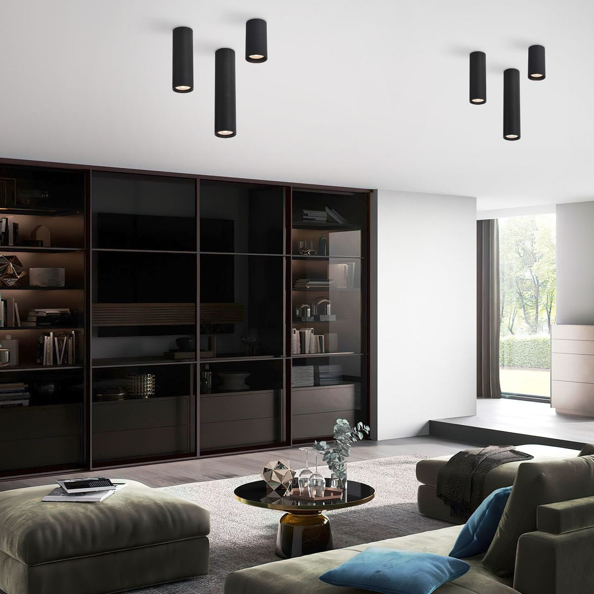Lampa sufitowa Tune L w kolorze czarnym, z trzema cylindrycznymi kloszami, zamontowana na suficie. W tle nowoczesne wnętrze z meblami i dużym oknem, na podłodze dywan, stół z dekoracjami i komfortowe kanapy.