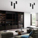 Lampa sufitowa Tune L w kolorze czarnym, z trzema cylindrycznymi kloszami, zamontowana na suficie. W tle nowoczesne wnętrze z meblami i dużym oknem, na podłodze dywan, stół z dekoracjami i komfortowe kanapy.