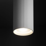 Lampa sufitowa Tune M w kolorze białym, z oprawą w formie cylindrycznego klosza z pionowymi żłobieniami. Ujęcie z bliska na dolną część lampy z widoczną żarówką GU10. Prosta forma, idealna do nowoczesnych wnętrz.