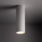 Biała lampa sufitowa Tune M z jednym miejscem na żarówkę GU10, o cylindrycznym kształcie z teksturą pionowych żłobień, zamontowana na suficie, emitująca ciepłe światło.