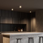 Lampa sufitowa Orion 1xGU10 w kolorze złotym, zamontowana na suficie w nowoczesnej kuchni. Widoczny minimalistyczny design oraz dwa źródła światła, oświetlające ciemne drewniane szafki. Tło w odcieniach szarości i drewna, z betonowym blatem.