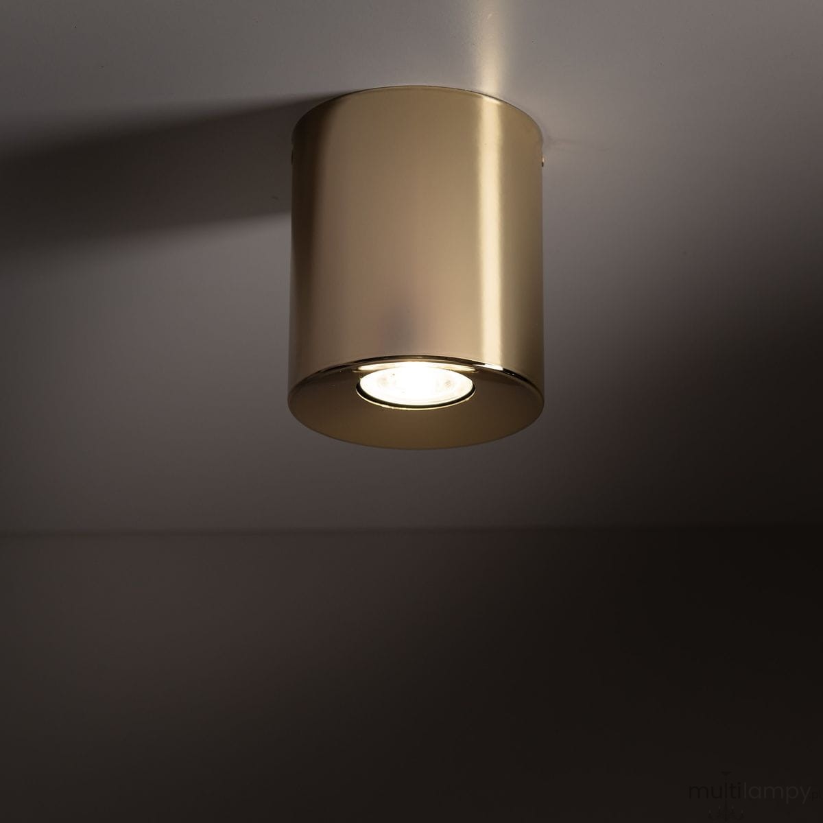 Złota lampa sufitowa Orion z jedną oprawą GU10, w cylindrycznym kształcie. Montowana do sufitu, emitująca jasne światło. Gładka, błyszcząca powierzchnia podkreśla elegancki wygląd.