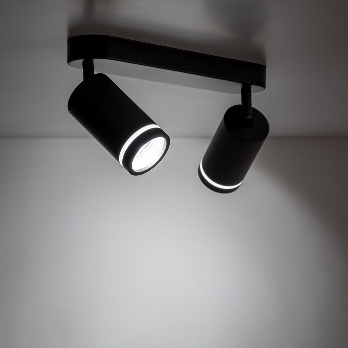 Jet lampa sufitowa (spot) z dwoma kloszami GU10 w kolorze czarnym. Klosze mają cylindryczny kształt z delikatnym podświetleniem. Produkt zamontowany na prostokątnej podstawie, widoczny z perspektywy frontalnej na jasnym tle.