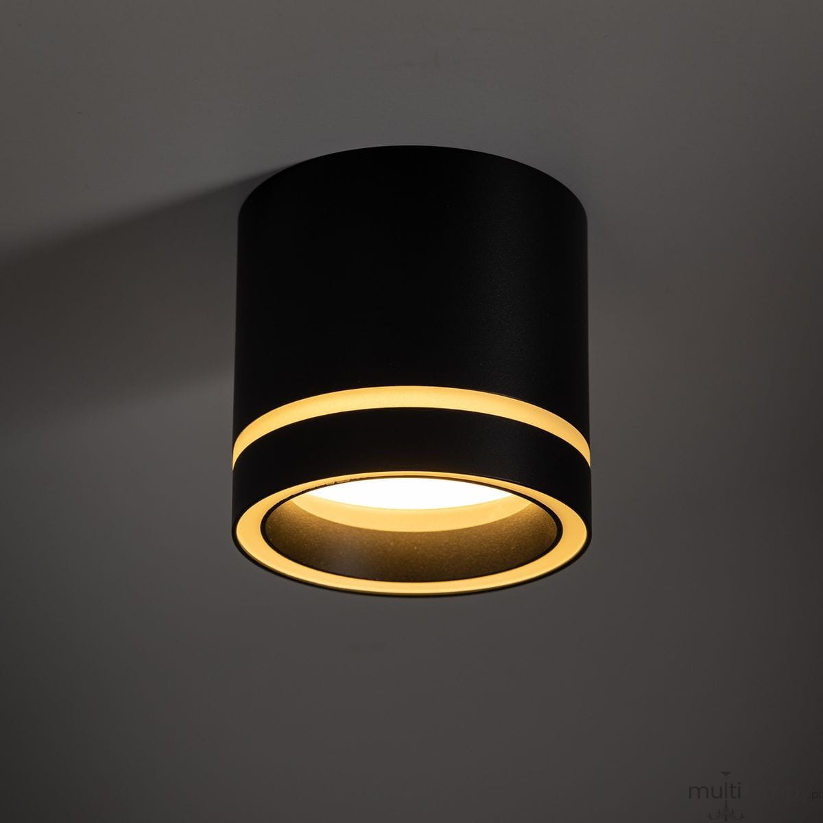 Czarna lampa sufitowa Jet z oprawą GX53, okrągła, z widocznymi dwoma złotymi pierścieniami dekoracyjnymi. Ujęcie z dołu ukazuje elegancki, minimalistyczny design i źródło światła w centrum.