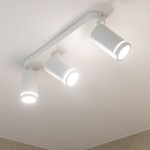Lampa sufitowa Jet z trzema reflektorami GU10 w białej obudowie. Reflektory o cylindrycznym kształcie, zamontowane na prostokątnej podstawie. Ujęcie z dołu, ukazujące włączone źródła światła. Tło jasne, minimalistyczne.