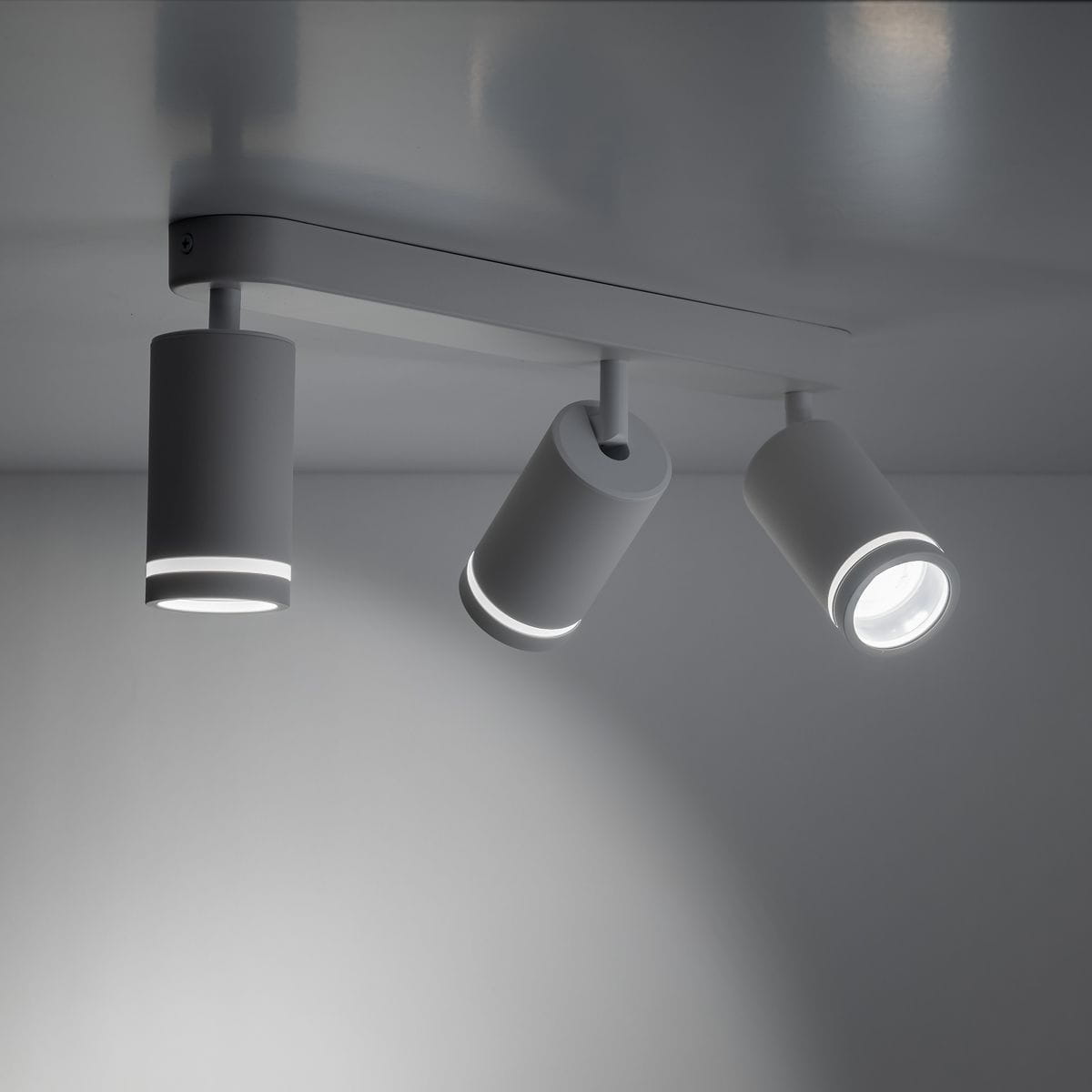 Lampa sufitowa Jet w białym kolorze, składająca się z trzech reflektorów na metalowej podstawie. Reflektory mają okrągłe kształty z podświetleniem na brzegach, zamontowane prostopadle do sufitu.