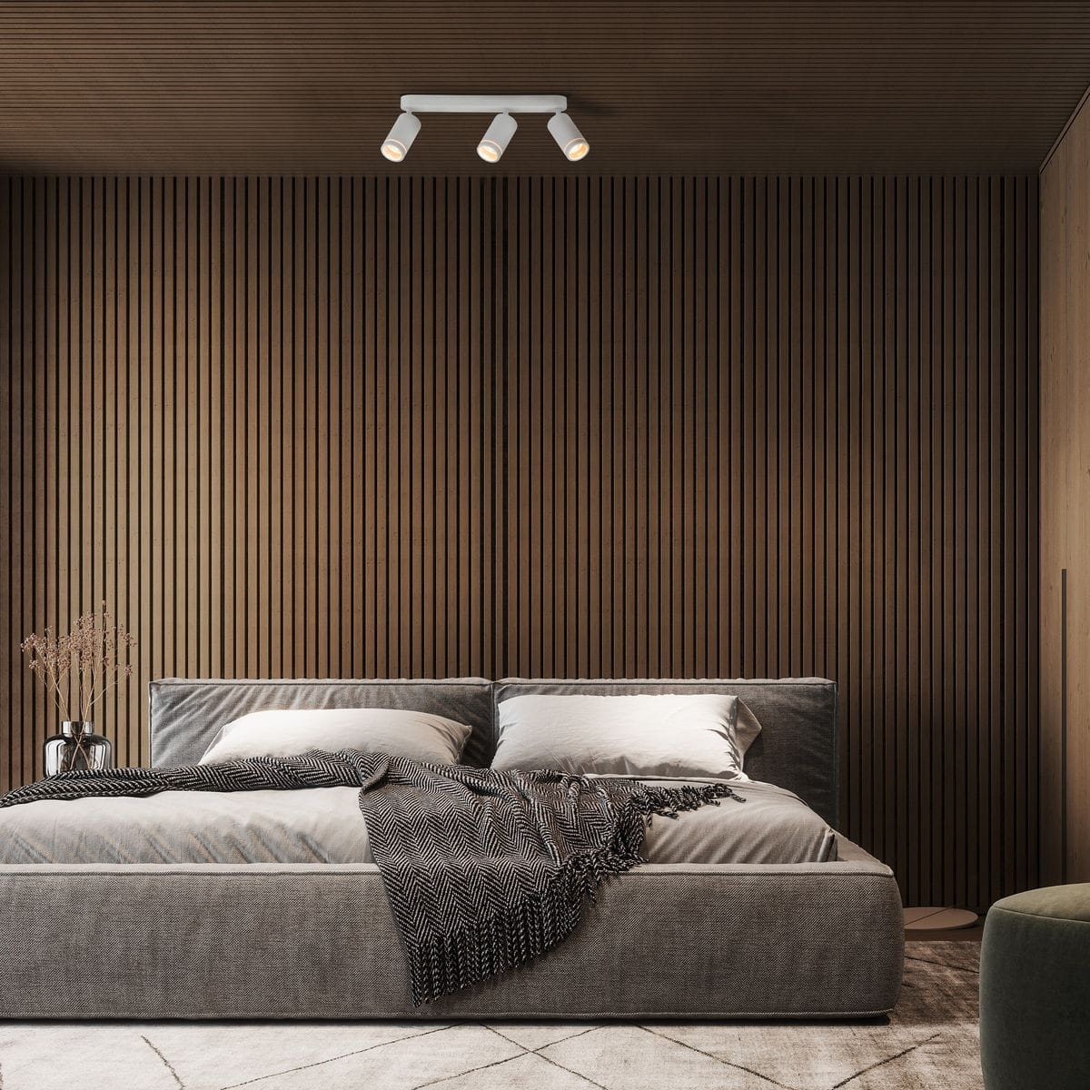 Lampa sufitowa Jet z trzema reflektorami GU10, w kolorze białym, zamontowana na drewnianym, poziomym tle. Oświetlenie skierowane w dół, idealne do nowoczesnych wnętrz. W tle widoczna tapicerowana łóżko z poduszkami i pledem.