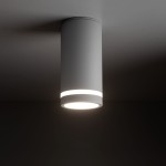 Lampa sufitowa Jet w kolorze białym, w kształcie cylindrycznym, z jedną oprawą GU10. Ujęcie z dołu pokazuje gładką fakturę obudowy oraz emitowane światło w dolnej części. Produkt zamontowany na suficie, tło ciemne.