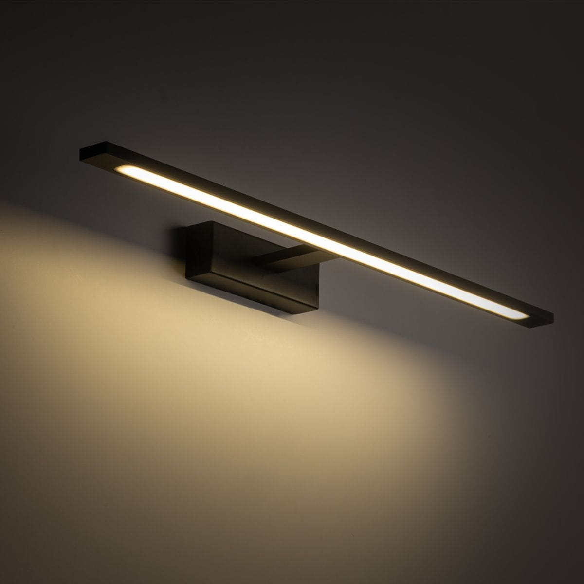 Kinkiet Gallery IP44 w kolorze czarnym, z prostokątnym, minimalistycznym designem. Wyposażony w jedną diodę LED o mocy 20W, zamontowany na ścianie, emitujący ciepłe światło wzdłuż równoległej listwy. Tło w odcieniach szarości.