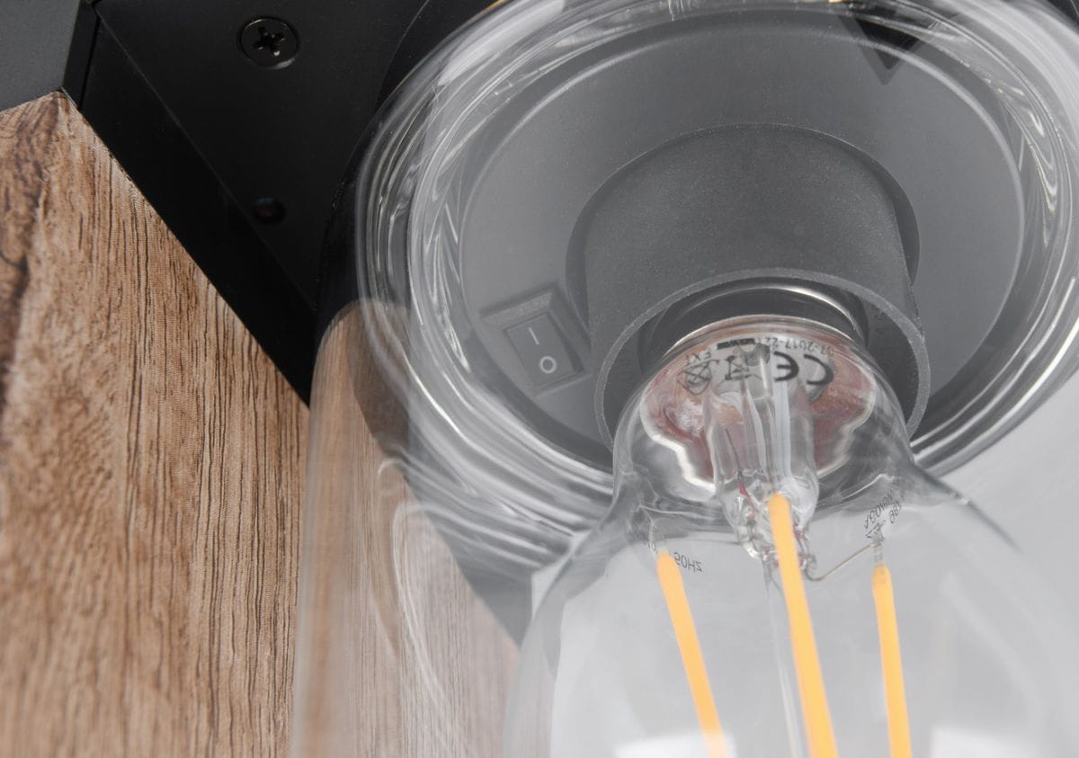 Lampa ogrodowa Ardila H100 z czujnikiem zmierzchu, stojąca, z oprawą imitującą drewno. Widok z bliska na detal żarówki E27 z widocznym włącznikiem. Kształt okrągły, przezroczysta osłona, ciemne elementy montażowe.