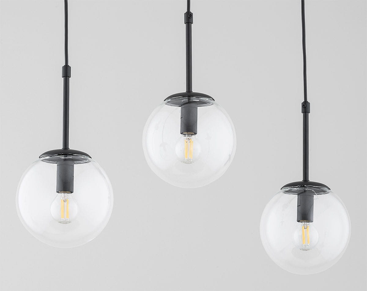 Lampa wisząca Sebia 3xE14 w kolorze czarnym, składająca się z trzech szklanych kul, zawieszonych na cienkich czarnych linkach. Kule mają przezroczyste wykończenie z widocznymi żarówkami E14 wewnątrz. Tło jasnoszare, proste.