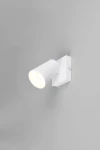 Kinkiet Sharp w kolorze białym z pojedynczym źródłem światła GU10. Lampa ma cylindryczny kształt klosza oraz prostokątną, montowaną na ścianie podstawę. Ujęcie z boku, ukazujące pełną konstrukcję. Tło w odcieniu szarości.