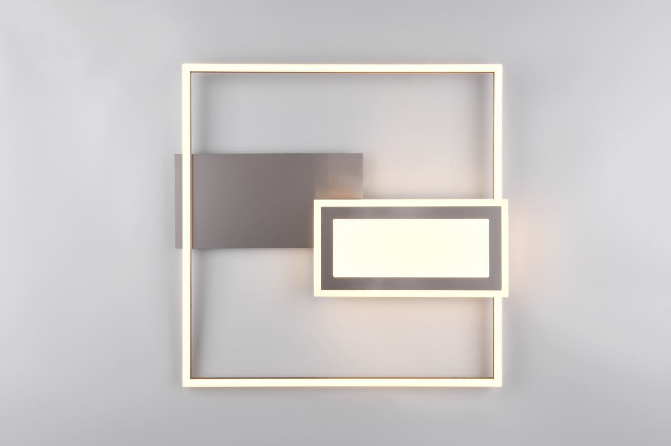 Lampa sufitowa Spiro w kolorze niklu, z dwiema diodami LED (32W). Ma nowoczesny, geometryczny kształt z prostokątnymi elementami oraz podświetleniem. Montowana na ścianie, z pilotem do zdalnego sterowania. Tło jasnoszare.