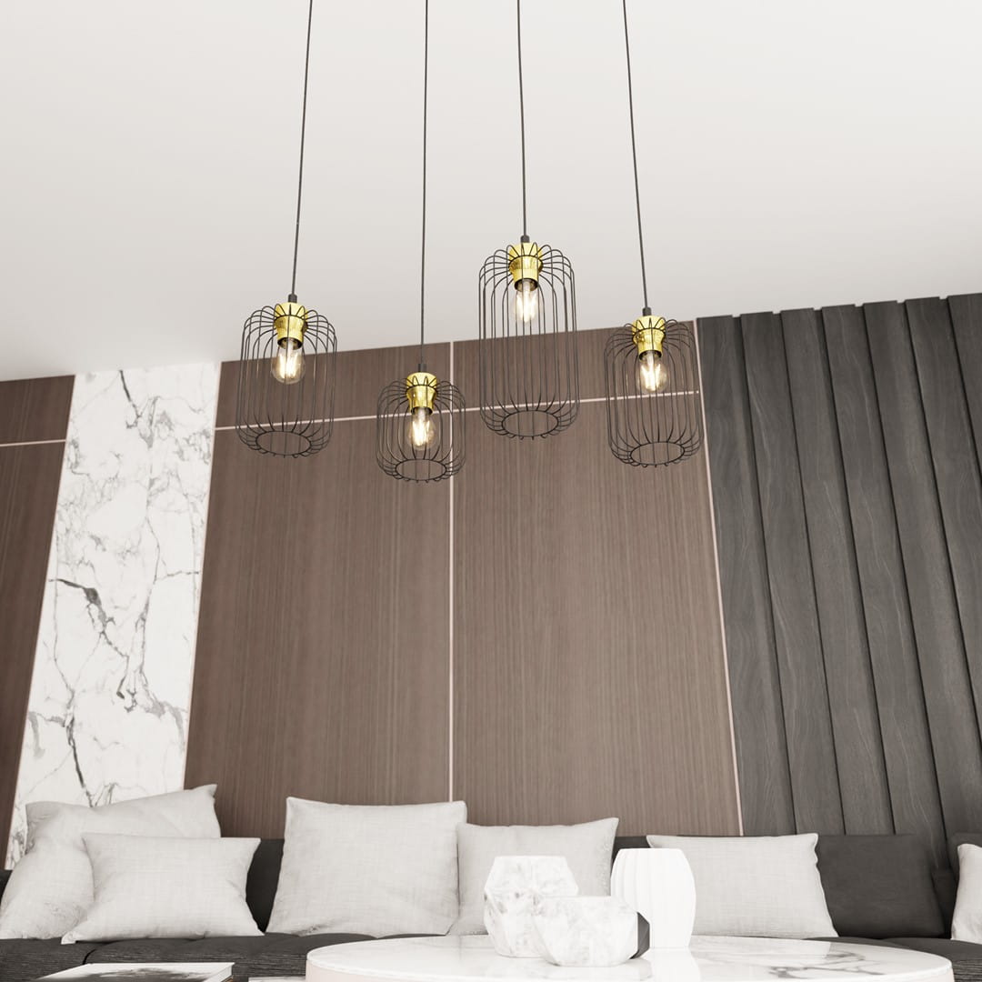 Lampa wisząca Vander 4 z czarnymi metalowymi kloszami w złotych detalach, zawieszona na długich linkach. Widoczne cztery żarówki w siatkach, umieszczona w nowoczesnym wnętrzu z drewnianą i marmurową ścianą oraz jasnymi poduszkami na kanapie.