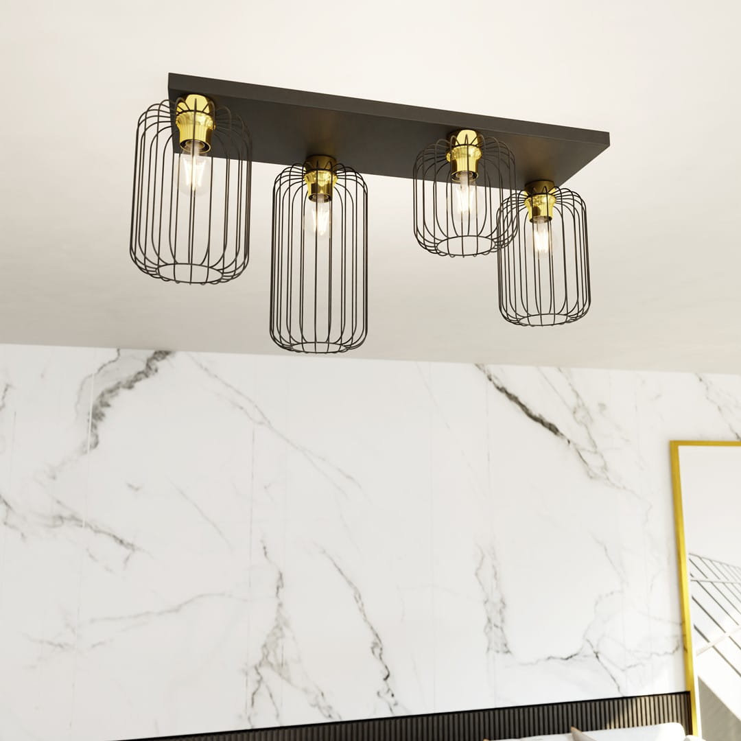 Czarna lampa sufitowa Barn 4GL z czterema kloszami w złotych oprawach. Klosze mają metalowe, siatkowe obudowy, a całość zamontowana jest na prostokątnej podstawie. Lampa wisi na jasnym tle z marmurowym wzorem.
