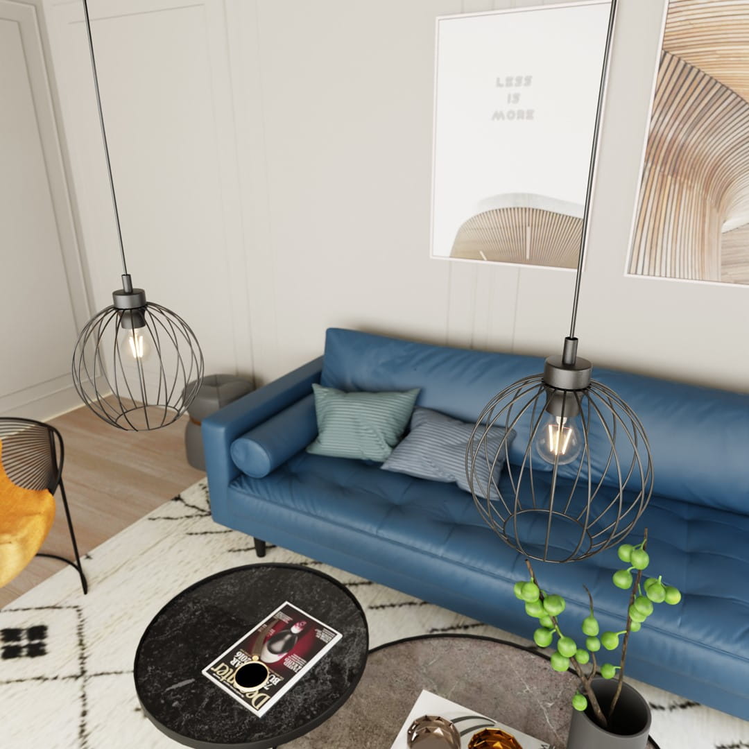 Czarna lampa wisząca Nando 1BL z oprawą na żarówkę E27, w formie okrągłej klatki. Zawieszona na cienkim przewodzie, znajduje się nad niebieską sofą z poduszkami. W tle widoczny stół kawowy z czasopismami i rośliną.