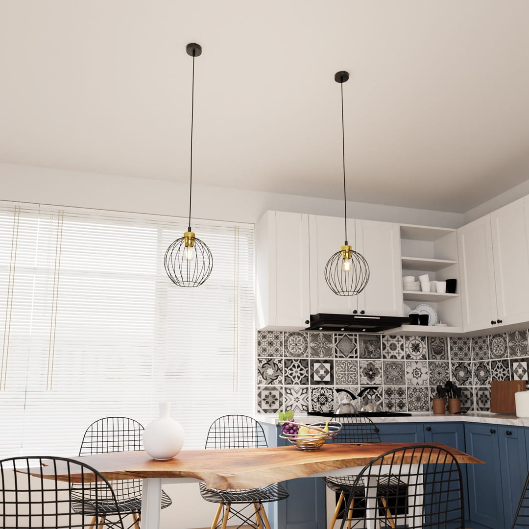 Lampa wisząca Nando 1GL w kolorze czarno-złotym, zawieszona na długim przewodzie. Posiada metalową, okrągłą konstrukcję z siatki, umieszczoną nad stołem w kuchni. W tle białe meble i kolorowa, wzorzysta kafelki.