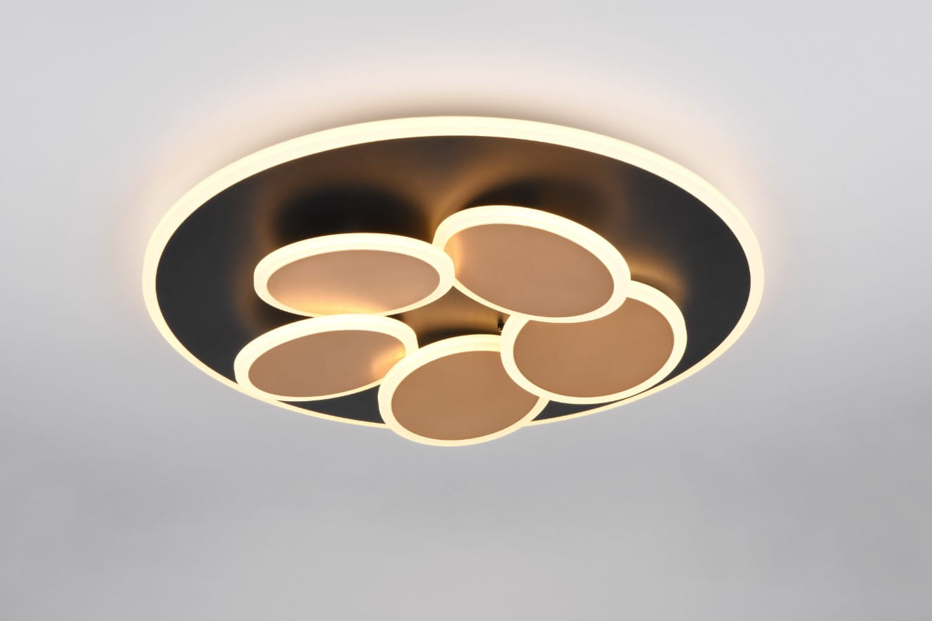 Czarna lampa sufitowa Mandala z pilotem, z pięcioma okrągłymi źródłami światła w złotych oprawach. Produkt zamontowany na suficie, z delikatnym podświetleniem. Stylowy design, idealny do nowoczesnych wnętrz.