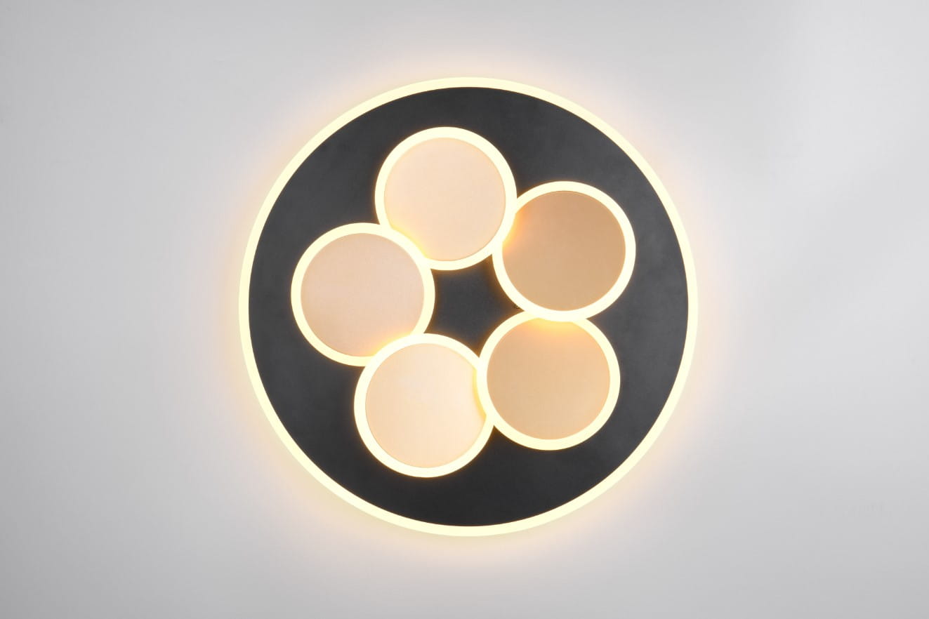 Lampa sufitowa Mandala w kolorze czarnym i złotym, z sześcioma okrągłymi kloszami LED, zamontowana na ścianie. Klosze mają matową powierzchnię, a lampa emituje ciepłe światło. Widoczny także pilot do zdalnego sterowania.