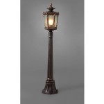 Lampa stojąca ogrodowa Amur 1-punktowa z metalowym słupkiem w ciemnym kolorze. Szklany klosz w kształcie latarni z widoczną żarówką, umieszczony na eleganckiej podstawie. Ujęcie frontalne, na szarym tle, podkreślające detale konstrukcji.