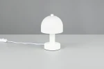 Lampa stołowa Glenn w białym kolorze, z okrągłym kloszem i prostą, cylindryczną podstawą. Ujęcie frontalne, lampa stoi na szarej powierzchni, z widocznym przewodem zasilającym. Idealna do nowoczesnych aranżacji wnętrz.