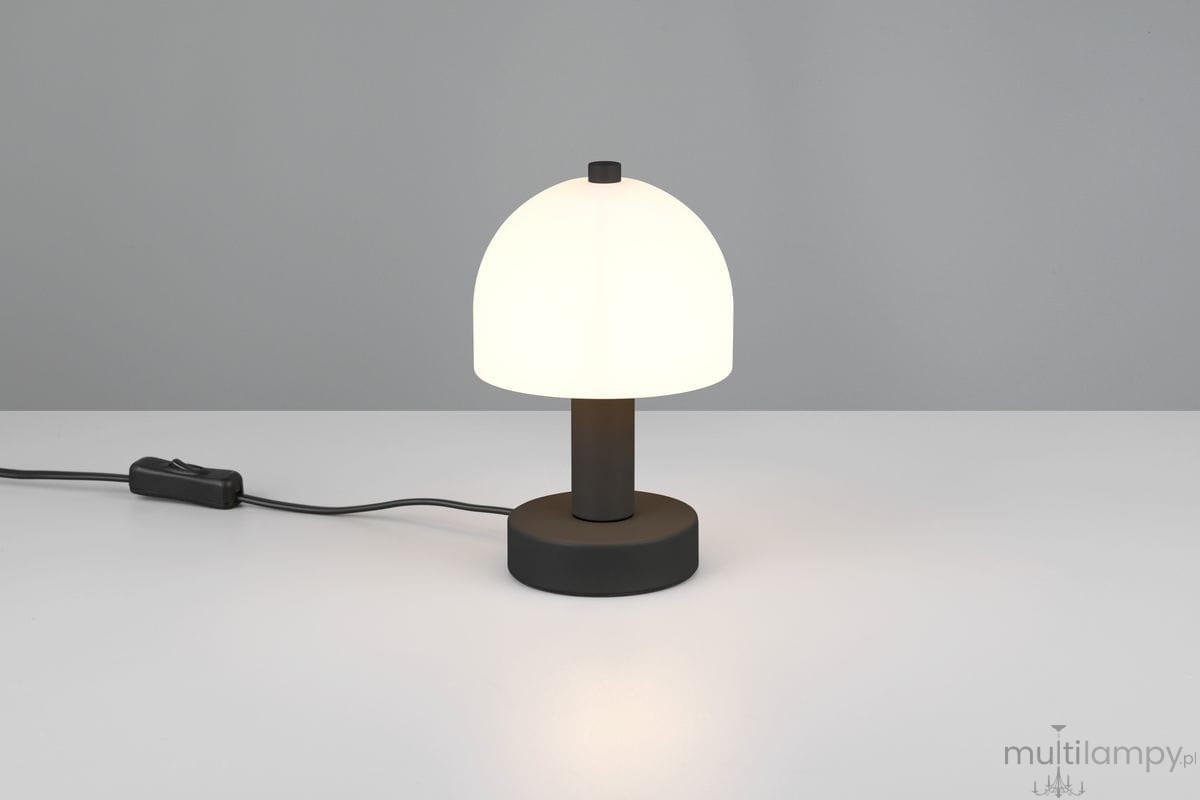 Lampa stołowa Glenn w kolorze czarnym z białym kloszem w kształcie półkuli. Ustawiona na płaskiej powierzchni, z widocznym przewodem z włącznikiem. Prosta, nowoczesna forma z okrągłą podstawą.