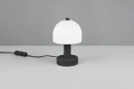 Czarna lampa stołowa Glenn z białym kloszem w kształcie półkulistym. Ustawiona na płaskiej powierzchni, z widocznym kablem z włącznikiem. Wysoka na około 30 cm, idealna do oświetlenia biurka lub stolika nocnego.