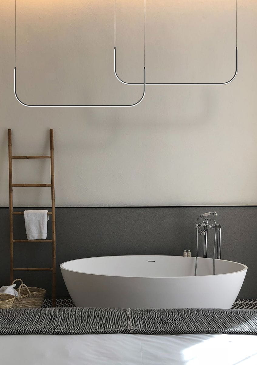 Lampa wisząca Minima 80 w kolorze czarnym, z jednym źródłem światła LED 20W. Zawieszona na cienkich linkach, ma minimalistyczny kształt. W tle widoczna wanna, drabina z ręcznikiem oraz strefa relaksu w nowoczesnej łazience.