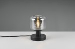 Lampa stołowa Mataro z czarną podstawą i przezroczystym kloszem, zamontowana na okrągłej podstawie. Widoczna żarówka E14, przyciągająca wzrok dzięki prostemu designowi. Kabel zasilający widoczny z boku, tło szare.