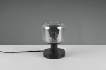 Czarna lampa stołowa Mataro z żarówką E14, z cylindrycznym kloszem z przezroczystego szkła. Ustawiona na okrągłej podstawie, z widocznym kablem zasilającym. Klosz odsłania źródło światła, tworząc nowoczesny akcent.