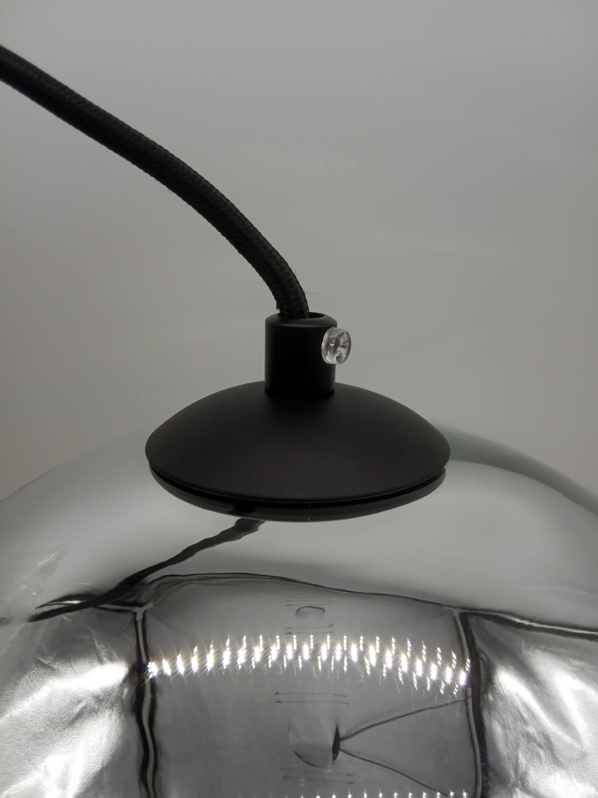 Lampa wisząca Mirror Glow D30 z chromowaną kopułą, zawieszona na czarnym, tekstylnym przewodzie. U góry widoczna czarna podsufitka z przezroczystym detalem. Odbicia światła na metalicznej powierzchni podkreślają elegancję.