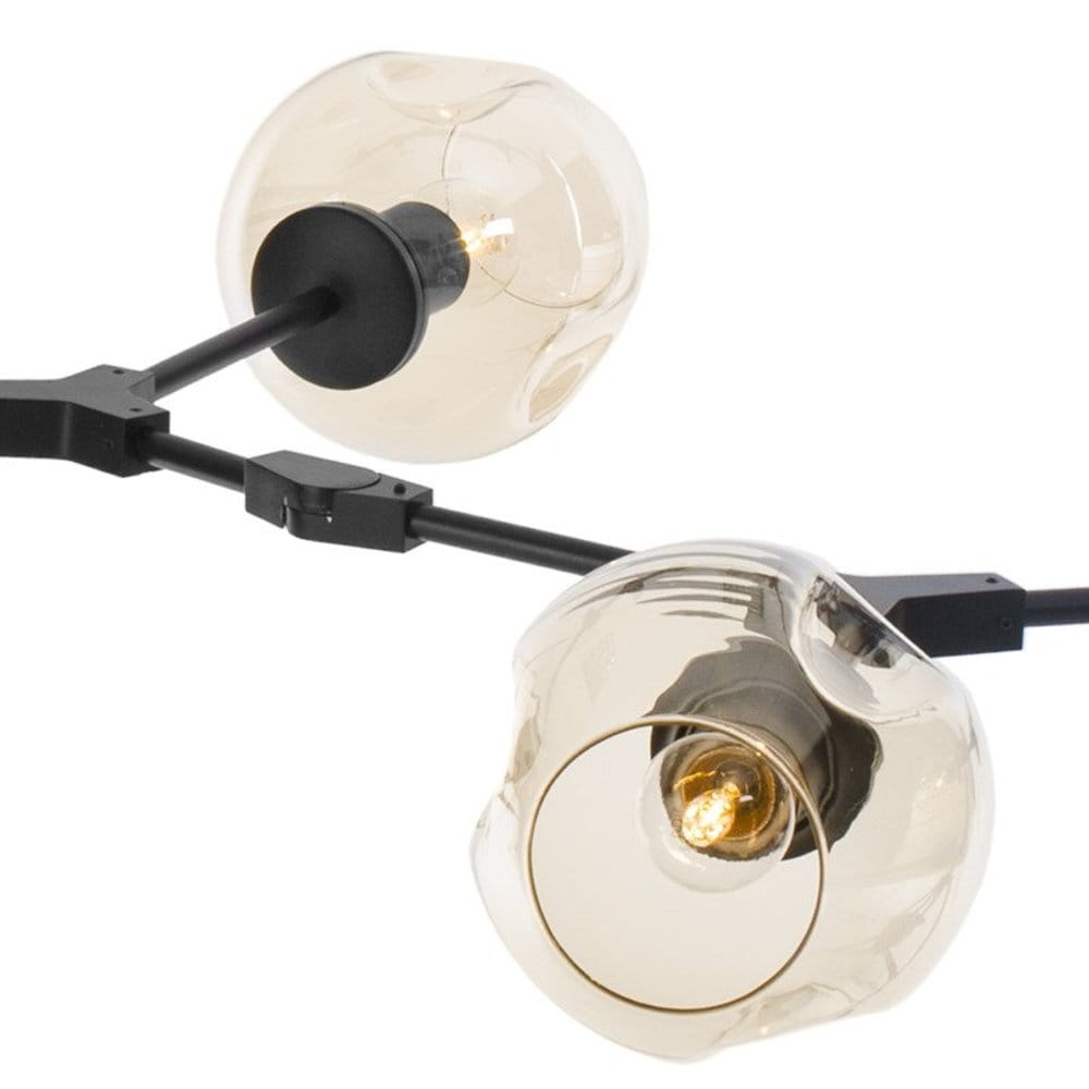 Lampa wisząca Modern Orchid z sześcioma oprawami E27, w kolorze czarnym i bursztynowym. Zbliżenie na szklane klosze o organicznych kształtach, zamocowane na czarnym stelażu. Widoczne żarówki emitujące ciepłe światło.